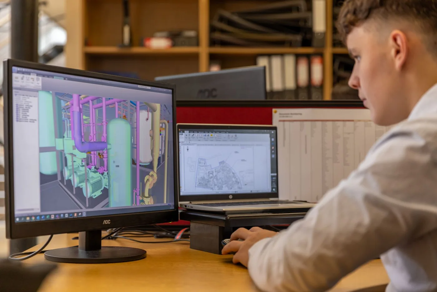 An engineer reviewing CAD drawings on two monitors.