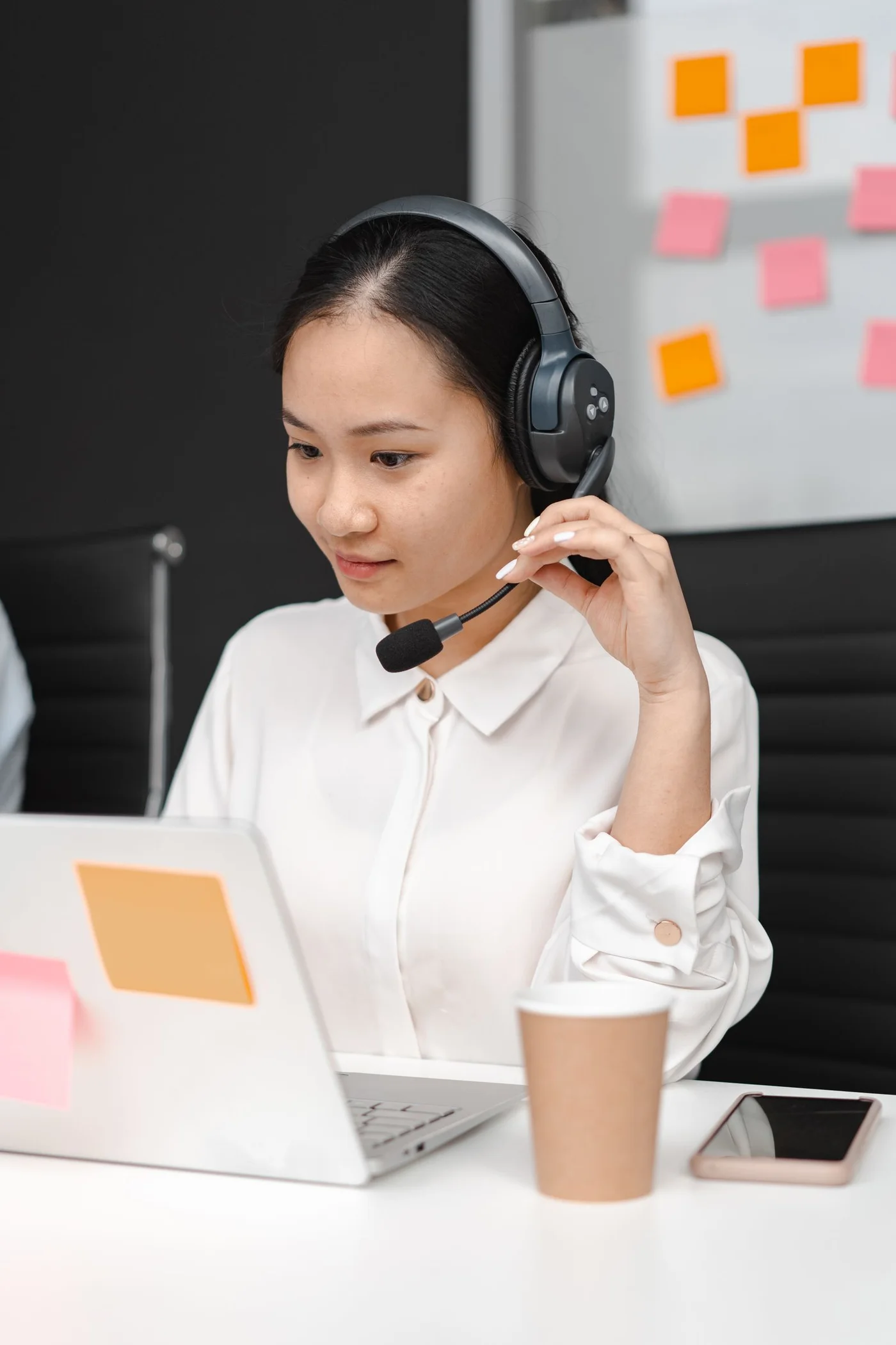 A woman assisting customers using a laptop and headset.