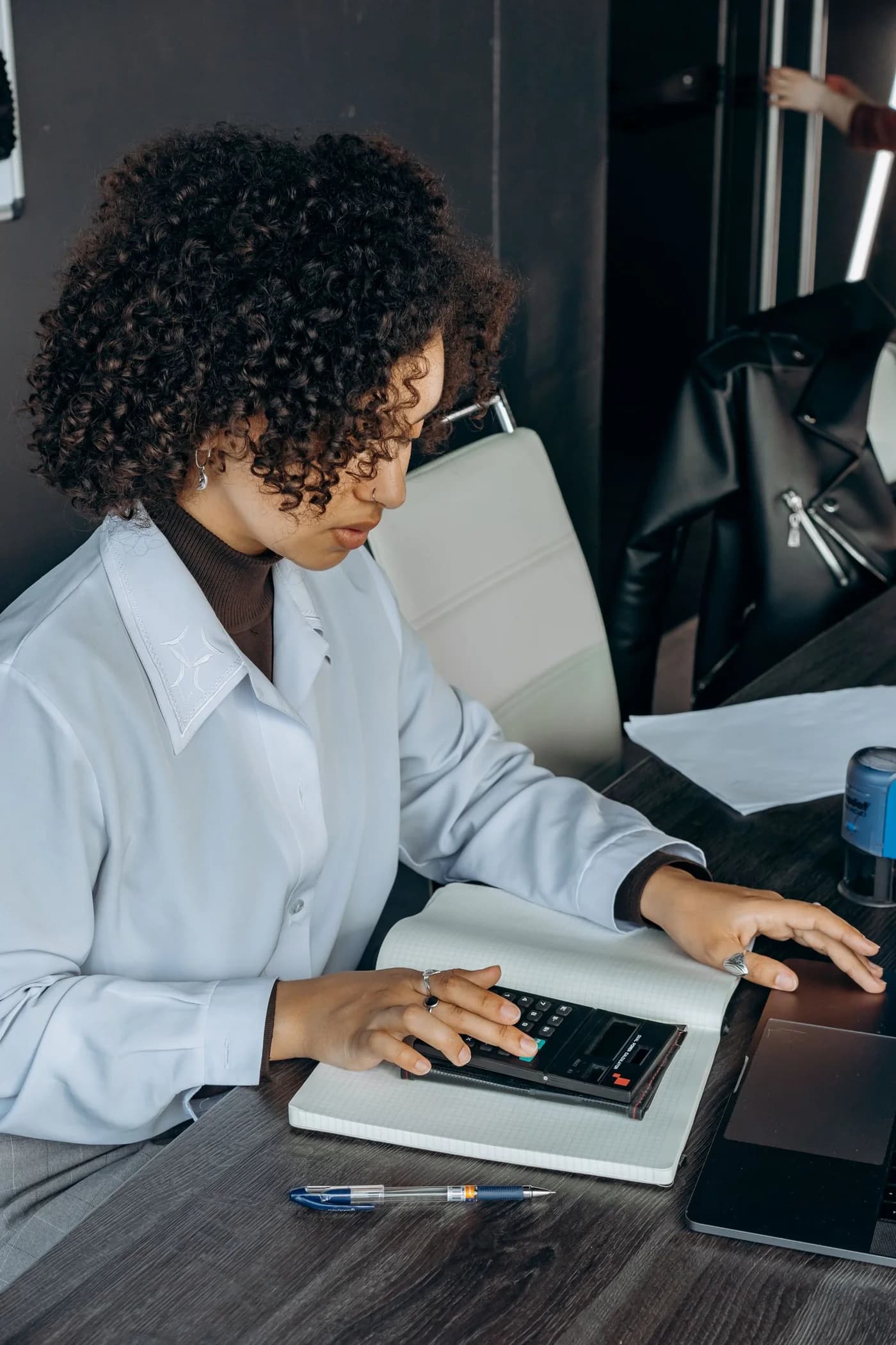 A woman using a calculator beside financial documents.
