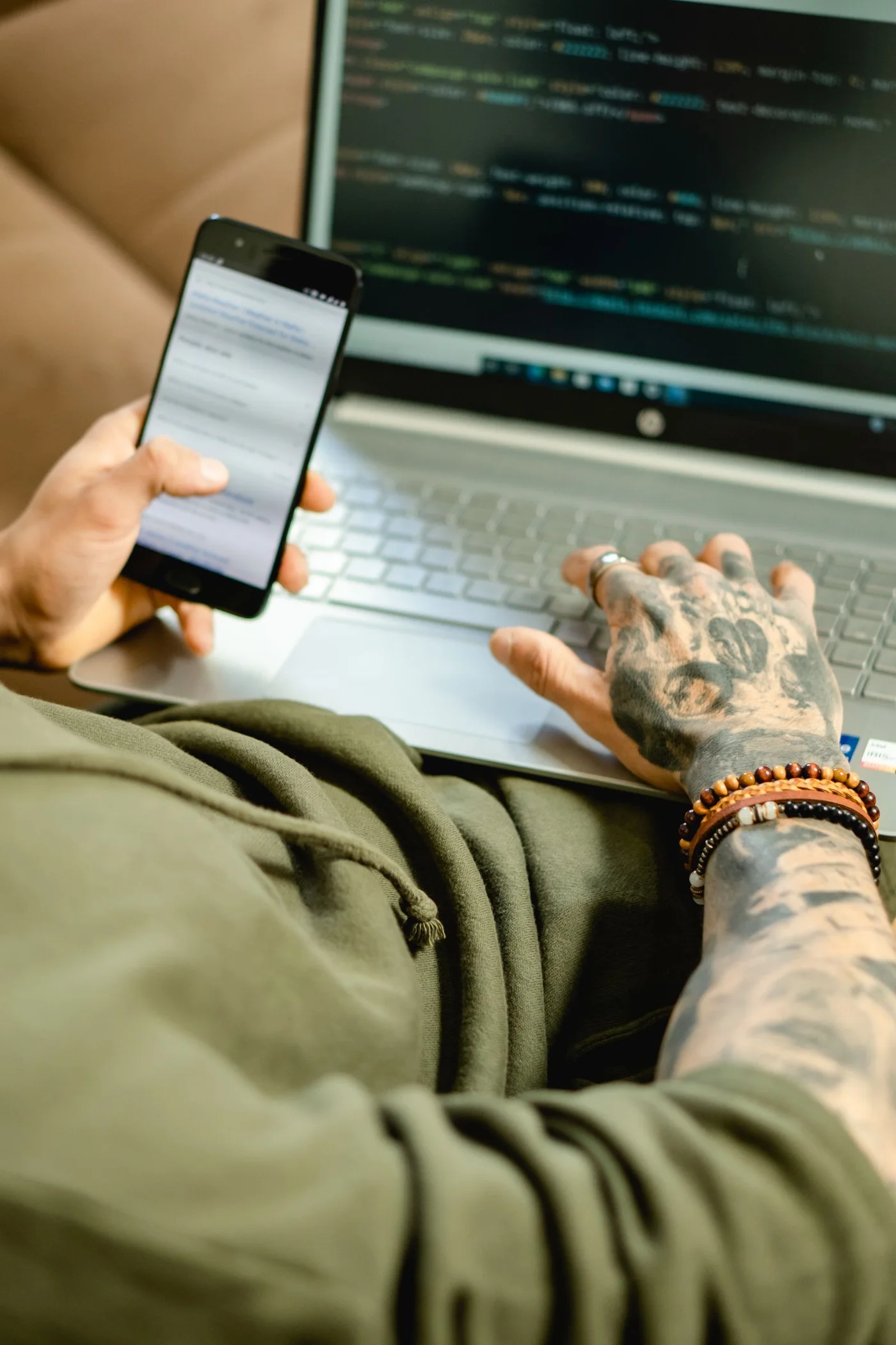 A professional checking a smartphone alongside a laptop.