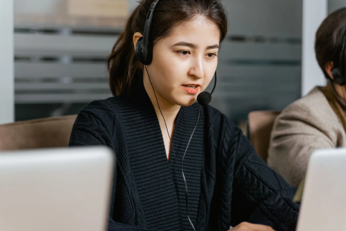A woman speaking through a headset while using a laptop.